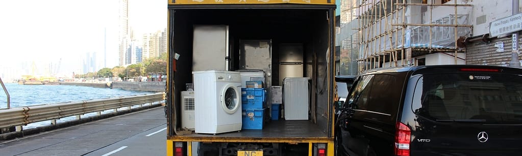 Hiring a moving company or moving things yourself - Picture of boxes, fridge, washing machine and items in the process of being moved to a new place in a hiring truck which is parked besides a Mercedes van.